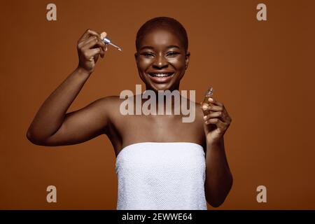 Nutrizione della pelle. Allegro e attraente biberon Black Woman con siero idratante viso Foto Stock