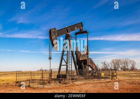 Grande vecchio cric pompa olio arrugginito circondato da recinzione pannello bestiame fuori in campo con cielo molto blu in inverno. Foto Stock