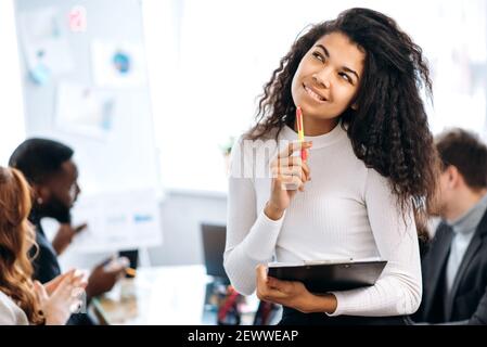 Bella donna di affari pensiva che pensa alle idee per un progetto, guardando il lato. Donna afroamericana che lavora su un nuovo progetto o sulla start-up alla conferenza con i suoi colleghi Foto Stock