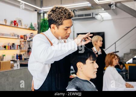 Cliente asiatico maschio che ottiene i capelli tagliati con il parrucchiere in salone. Barbiere alla moda usando una forbice per tagliare i capelli del cliente in barbiere Foto Stock