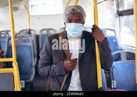Uomo anziano afro-americano che indossa una maschera facciale in piedi sull'autobus Foto Stock