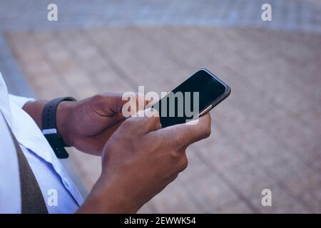 Sezione centrale dell'uomo afroamericano che sta nella strada usando smartphone Foto Stock