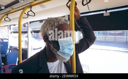 Uomo anziano afro-americano che indossa una maschera facciale in piedi sull'autobus guardando fuori dalla finestra Foto Stock
