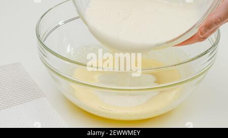 Cottura. Bianchi montati mescolando con i tuorli montati in una ciotola di vetro, sfondo bianco della tavola di kicthen Foto Stock