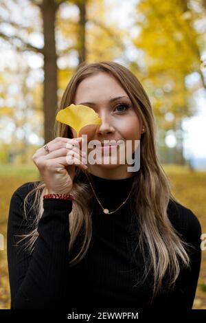 Una giovane bionda si trova sotto un baldacchino di gingko alberi in autunno Foto Stock