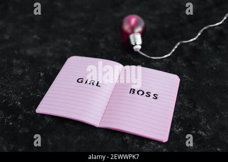 Pari opportunità Girl Boss testo in cima al notebook rosa con lampadina rosa brillante simbolo di idee e inventiva su sfondo nero Foto Stock