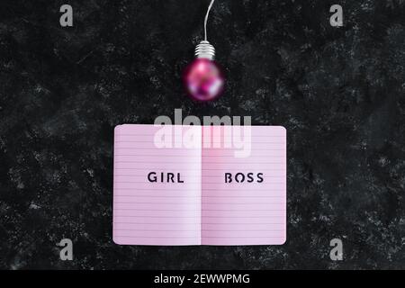 Pari opportunità Girl Boss testo in cima al notebook rosa con lampadina rosa brillante simbolo di idee e inventiva su sfondo nero Foto Stock