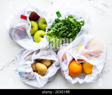 Frutta e verdura estiva in sacchetti riutilizzabili eco-friendly mesh su sfondo marmoreo. Shopping senza sprechi. Concetto ecologico. Foto Stock