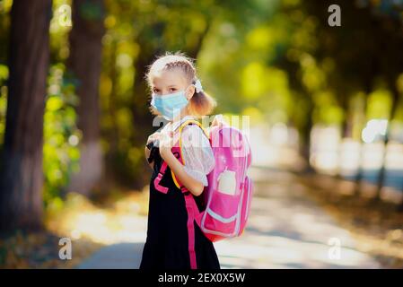 Ragazza della scuola che indossa maschera e zaino per proteggere dal coronavirus. Il bambino va a scuola dopo la pandemia oltre. Foto Stock