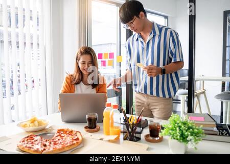 Felici lavoratori del team aziendale che parlano di progetto e di condividere il pasto godendo di divertirsi al lavoro avendo riunione mangiare pizza e patatine. Foto Stock