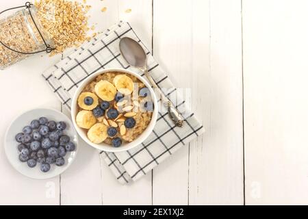 Vista dall'alto della ciotola di farinata d'avena con mirtillo e banana a fette su un tavolo di legno. Spazio di copia, Foto Stock