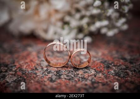 Arrangiamento floreale con fiori bianchi, bouquet di nozze con un nastro e due anelli d'oro, sdraiati su una pietra. Decorazioni per matrimoni, opere d'arte, fioraio Foto Stock