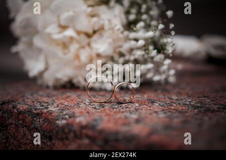 Arrangiamento floreale con fiori bianchi, bouquet di nozze con un nastro e due anelli d'oro, sdraiati su una pietra. Decorazioni per matrimoni, opere d'arte, fioraio Foto Stock