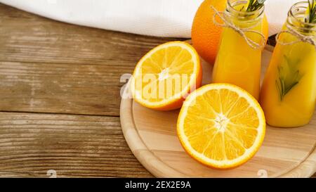 Succo d'arancia in bottiglie di vetro. Il succo è decorato con uno sprig di rosmarino. Succo su sfondo di legno con asciugamano bianco Foto Stock