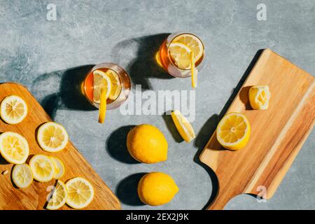 vista dall'alto dei bicchieri con cocktail alcolico e limone accanto ai limoni sulle tavole su sfondo grigio Foto Stock