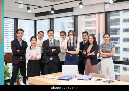 Gruppo d'affari multietnico sicuro che attraversa le armi in un ufficio moderno nel quartiere degli affari Foto Stock