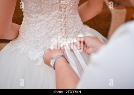 Abito da sposa, corset. La mamma stringe un arco sull'abito della sposa. Foto Stock