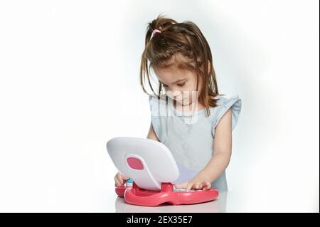 Bambina che usa un computer portatile giocattolo isolato su sfondo bianco dello studio Foto Stock