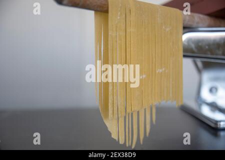 Linguine di pasta fatta in casa appesa su bastone di legno per asciugare. Tagliatelle italiane fatte in casa appese su un bastone di essiccazione della pasta. Foto Stock