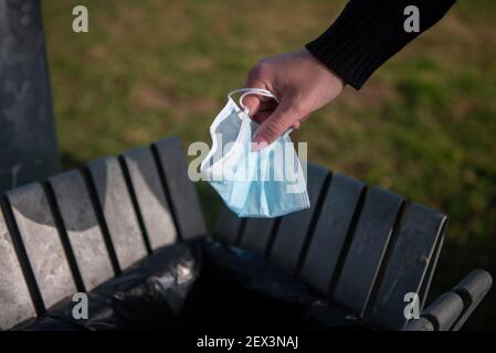 Primo piano del braccio di una donna che sta gettando una maschera chirurgica nel bidone per prevenire la diffusione di covid 19 o coronavirus. Foto Stock