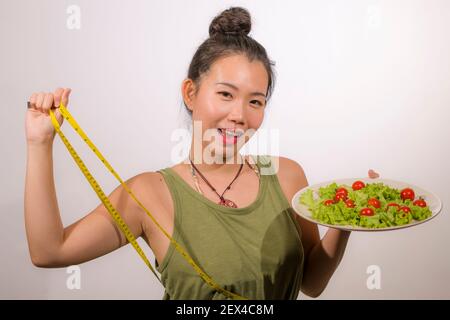 Benessere e cura di sé - giovane felice e bella asiatica Donna coreana che tiene piatto con lattuga e pomodori ciliegini sorridenti allegro in nurri sano Foto Stock