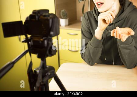 Una donna conduce una trasmissione vlog dal vivo, registra un video su una telecamera da casa. Comunicazione remota, nuova realtà, blog, videoconferenze Foto Stock