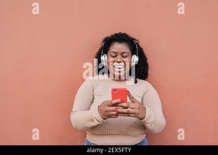 Ragazza africana curvy che ascolta musica da playlist mentre si guarda Sul telefono cellulare - Millennial ragazza che si diverte con la tecnologia Tendenze - Focus su fa Foto Stock