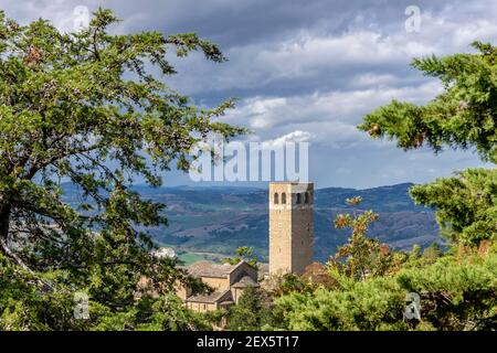 La Torre Civica di San Leo, Italia, incorniciata da rami di alberi, sotto un cielo drammatico Foto Stock