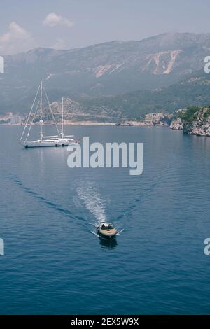 Una lussuosa barca a motore sportiva in legno fornisce i VIP da una grande barca bianca attraccata al largo della costa del Montenegro, vicino all'isola di Sveti Stefan, Budva Foto Stock