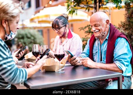 Persone mature che utilizzano smartphone con maschera a faccia aperta - anziani pensionati che guardano notizie positive su smartphone - Nuovo concetto di stile di vita normale Foto Stock