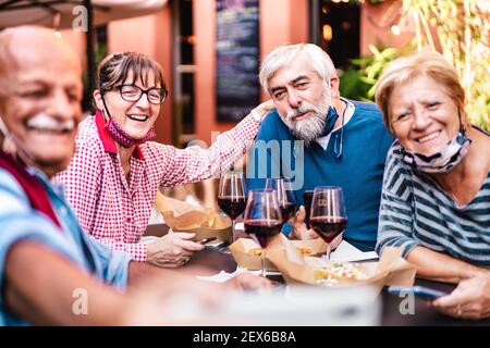 Amici anziani felici che prendono selfie al ristorante con faccia aperta Mask - i pensionati che si divertono insieme al winebar dopo riapertura blocco Foto Stock