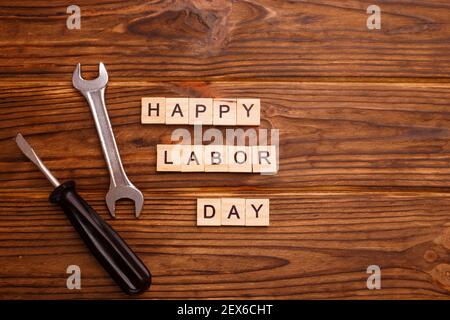 Concetto di biglietto d'auguri per il giorno del lavoro felice. HAPPY LABOR DAY testo in legno con strumenti su sfondo di legno. Disposizione piatta, vista dall'alto. Foto Stock