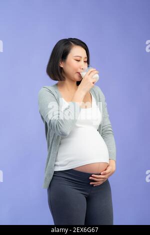 La madre incinta beve il latte su sfondo lilla Foto Stock