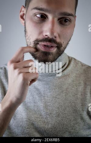 Ritratto di un giovane che graffia la barba con un dito mentre sta pensando a qualcosa Foto Stock