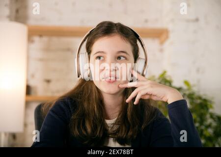 Bambina indossa le cuffie durante il corso di formazione online, la lezione, la vista dello schermo. Utilizzo delle cuffie. Concetto di utilizzo facile e comodo, formazione, online, infanzia, tecnologie moderne per la rimodellazione. Foto Stock