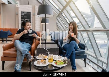 Coppia asiatica seduta e mangiando inn Airport lounge quando si attende il volo in un moderno aeroporto internazionale, viaggio e concetto di trasporto Foto Stock