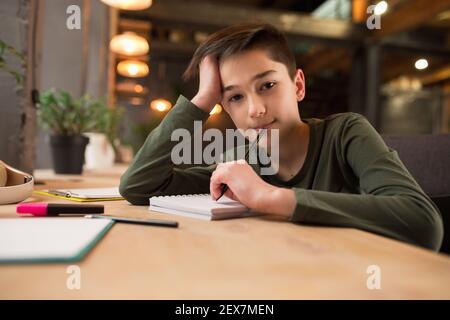 Bambino seduto al tavolo durante l'ascolto dell'insegnante su videocall online, corso di formazione, lezione online. Utilizzo di carta intestata. Concetto di utilizzo facile e comodo, formazione, online, infanzia. Foto Stock