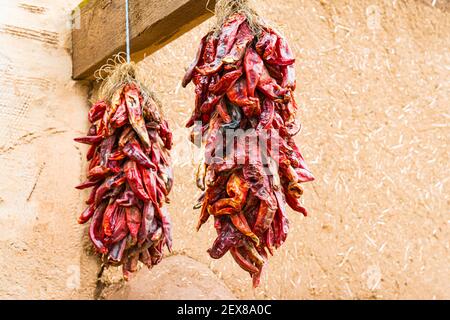 Due mazzi di peperoncini rossi secchi sospesi all'esterno Di un edificio di adobe in New Mexico Foto Stock