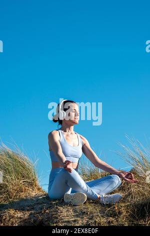 Donna che medita e ascolta musica fuori al sole. Indossare le cuffie. Foto Stock