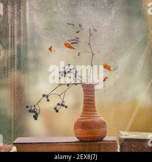 Sagome di rami secchi con bacche su davanzale con libri, finestra con gocce di pioggia, sfondo sfocato, fuoco selettivo. Concetto di autunno, stagione Foto Stock