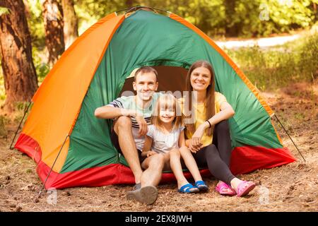 Famiglia di tre persone in campeggio e divertirsi insieme nella foresta estiva. Vacanze in campeggio. Foto Stock