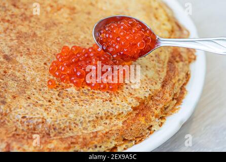 Pila di crepes o frittelle con caviale di salmone rosso in cucchiaio in cima. Concetto di Shrovetide. Foto Stock