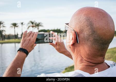 uomo di 65 anni che scatta una foto con uno smartphone in un parcheggio Foto Stock