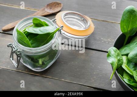 Foglie di spinaci in vaso di vetro su sfondo rustico di legno. Vista Closeup della ciotola con spinaci e cucchiaio di legno. Concetto di cibo sano. Foto Stock