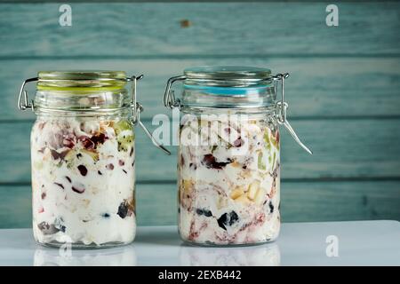 Due vasetti di yogurt fresco con frutta e bacche al suo interno su sfondo di legno blu. Foto Stock