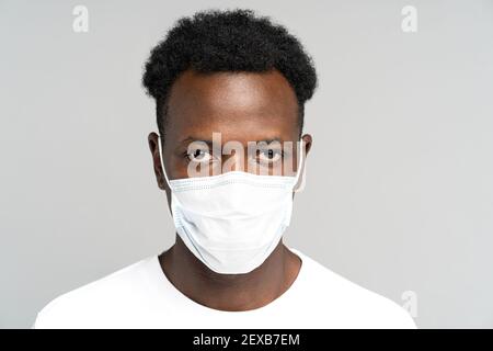 Giovane afroamericano che indossa maschera medica facciale, guardando la macchina fotografica, isolato su sfondo grigio Foto Stock