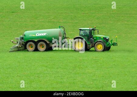 Trattore John Deere che lavora in un campo con pasta Conor autocisterna e barra di dribble che sparge liquame di fattoria di caseificio su un campo come fertilizzante naturale Foto Stock