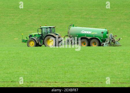 Trattore John Deere che lavora in un campo con pasta Conor autocisterna e barra di dribble che sparge liquame di fattoria di caseificio su un campo come fertilizzante naturale Foto Stock