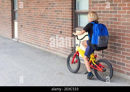 Bambino che va a scuola in bicicletta. Bicicletta da corsa per studenti vicino al muro dell'edificio scolastico. Foto Stock