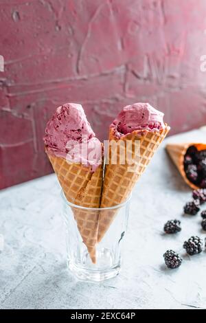 Due coni di waffle riempiti di gelato blackberry sono tenuti in un bicchiere, a forma di cuore. Foto Stock